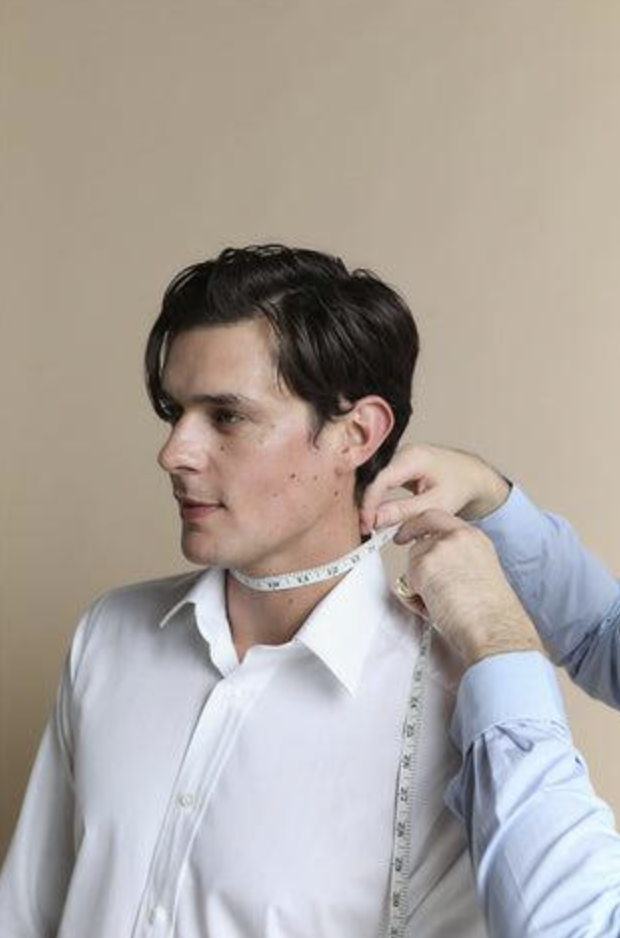 Man in white shirt having his neck measured with a tape measure by another person.