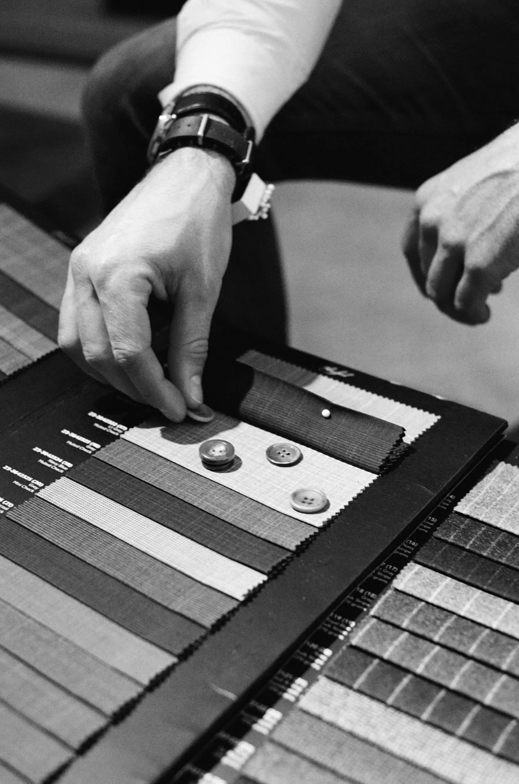 A person using a color swatch book to select fabric or material textures, with three buttons and a small white bead on the swatch.