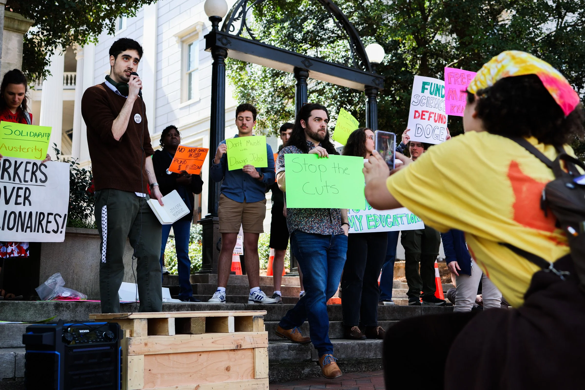 Moss Joslin, left, takes a photo of Rob Tabackman, right, while he addresses the crowd during the United Campus Workers protest in Downtown Athens, Georgia, on Mar. 19, 2025.  United Campus Workers held a protest on Mar. 19, 2025 in support of higher