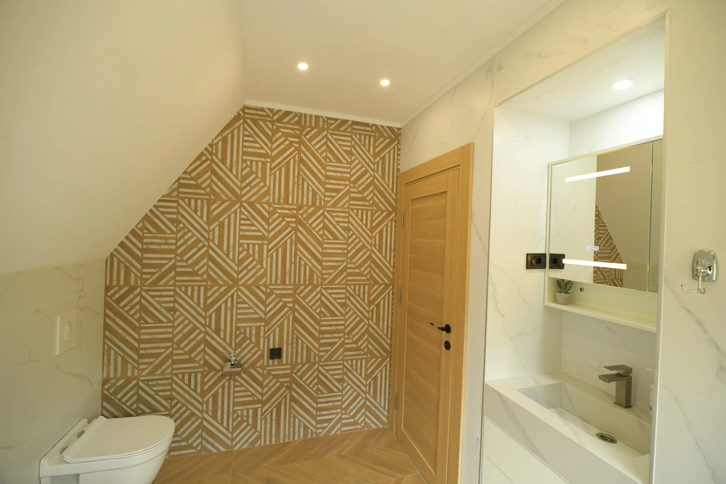 Bathroom with geometric patterned wall tiles, a wooden door, a mirror, a sink, and a toilet.