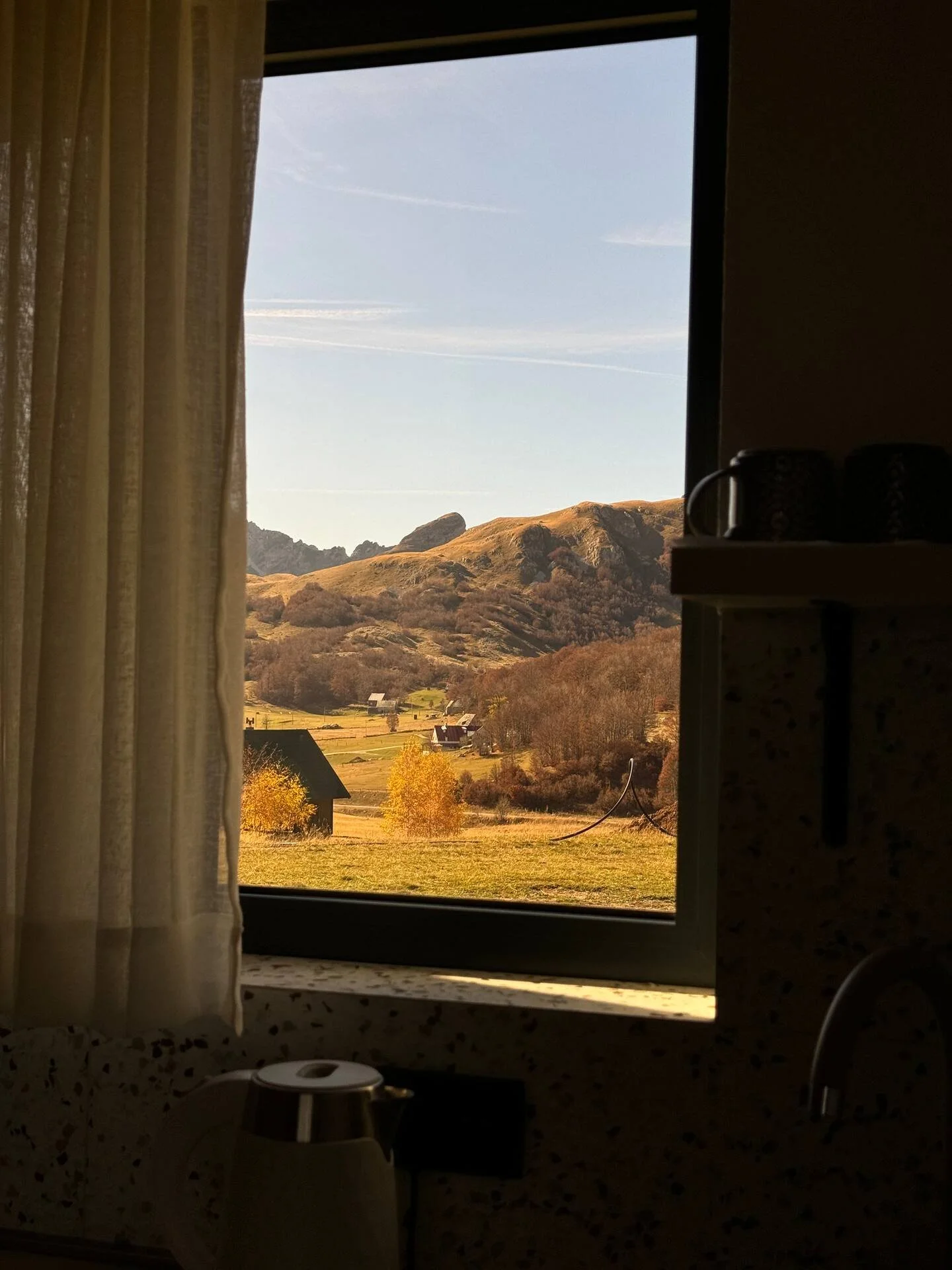 View of a mountainous landscape through a kitchen window, with houses and trees in the foreground.