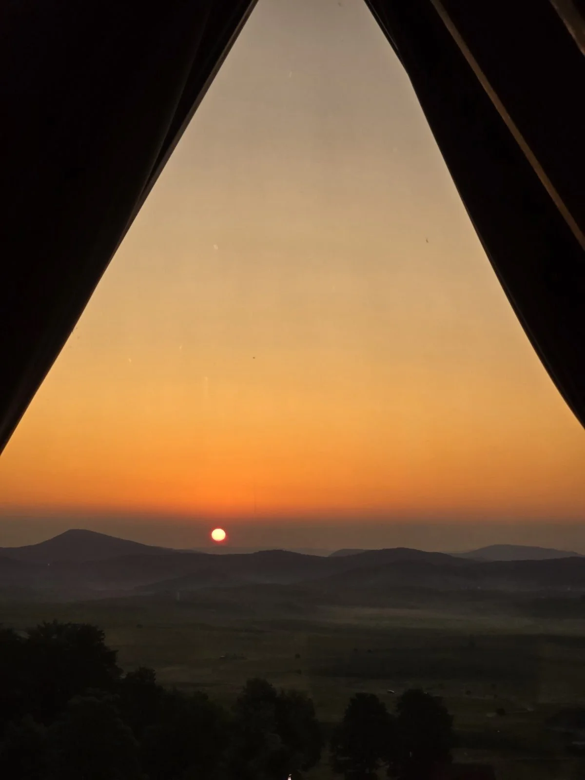 Sun setting over rolling hills seen through a tent window during sunset.