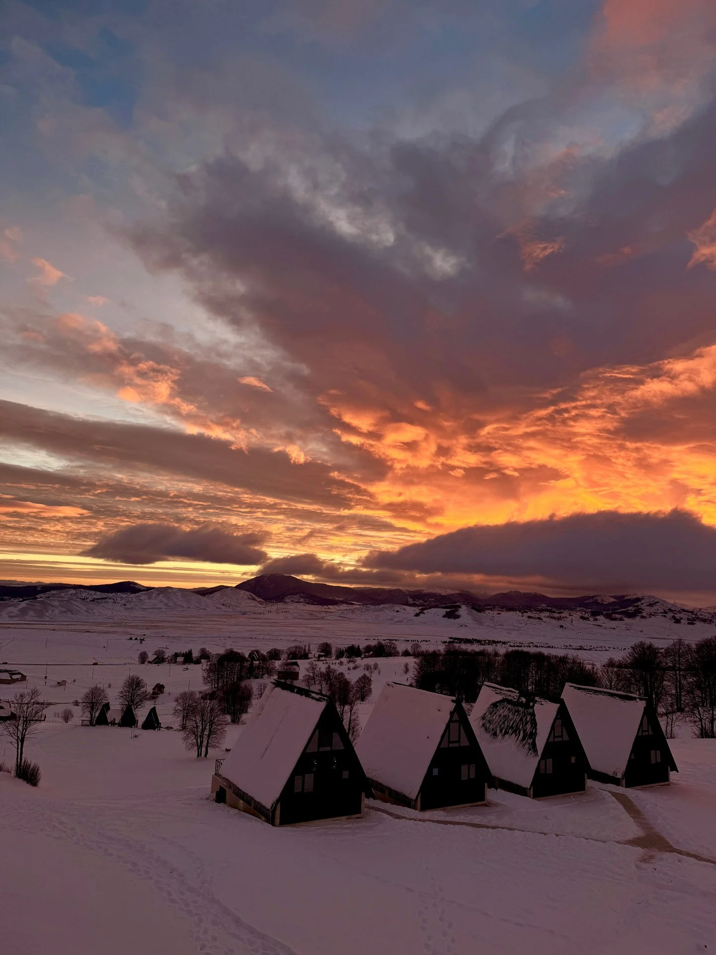 Snow-covered landscape with four A-frame cabins under a colorful sunset sky.