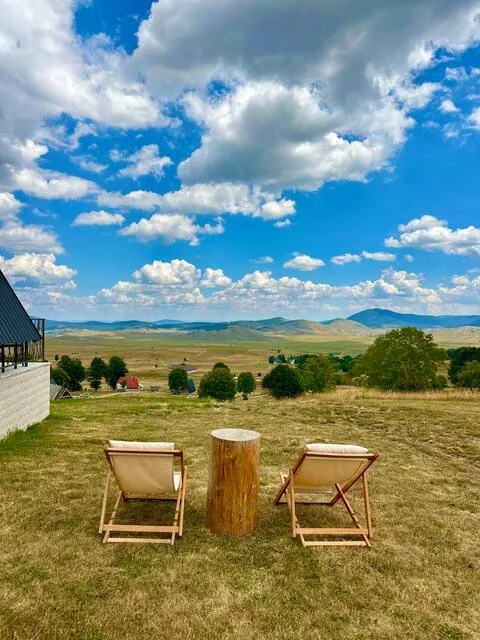 Two lounge chairs facing a scenic open field with clouds in the sky and distant hills