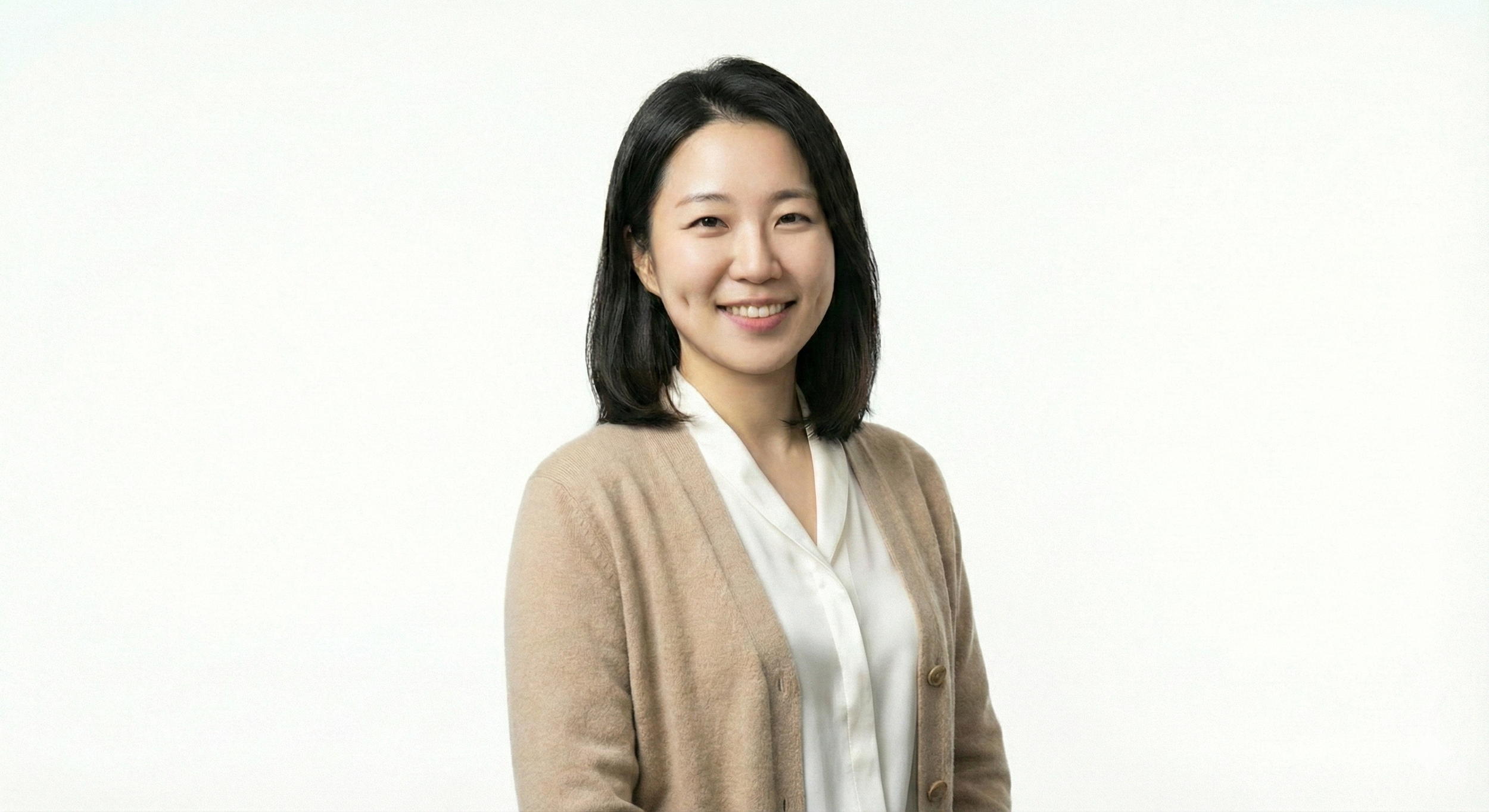 A woman with shoulder-length black hair, wearing a cream-colored cardigan over a white blouse, smiling at the camera against a plain white background.