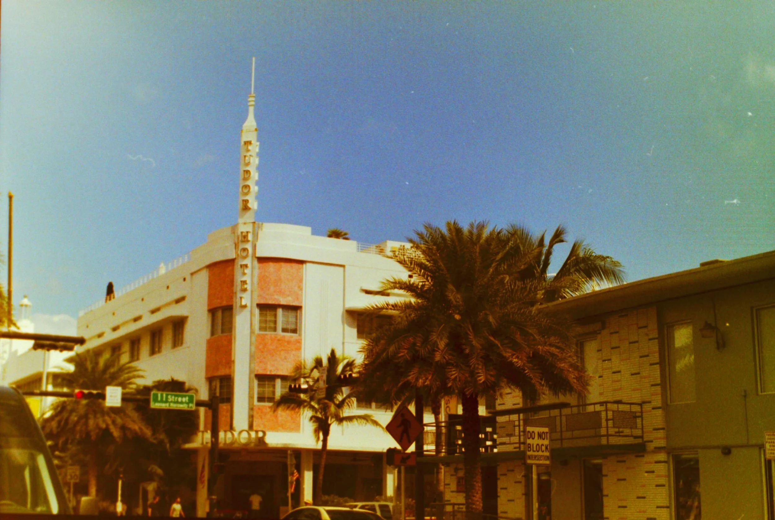 Vintage-toned photo of an Art Deco hotel with a spire, beside palm trees.