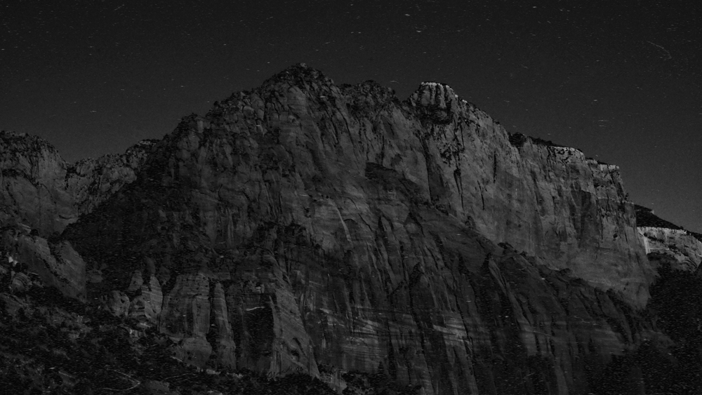 Black and white photo of a rocky mountain peak under a starry night sky.