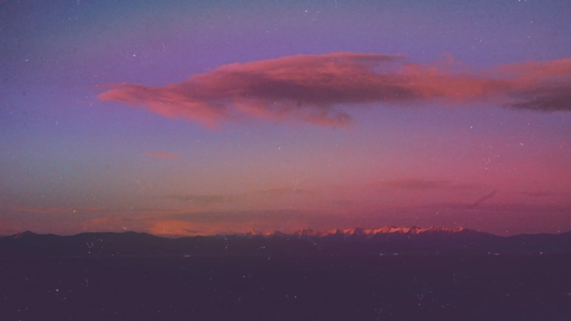 A mountain landscape during sunset or sunrise with pink and purple clouds in the sky.