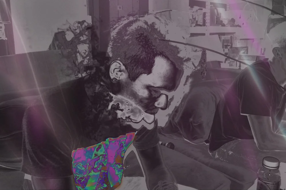 A man in sunglasses leaning over a table, in grayscale with a colorful patterned patch.