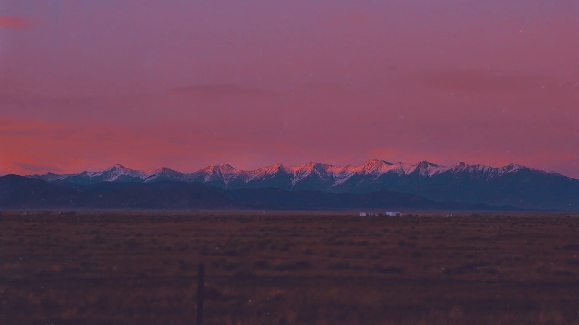 Sunset over snow-capped mountains with a pink and purple sky.