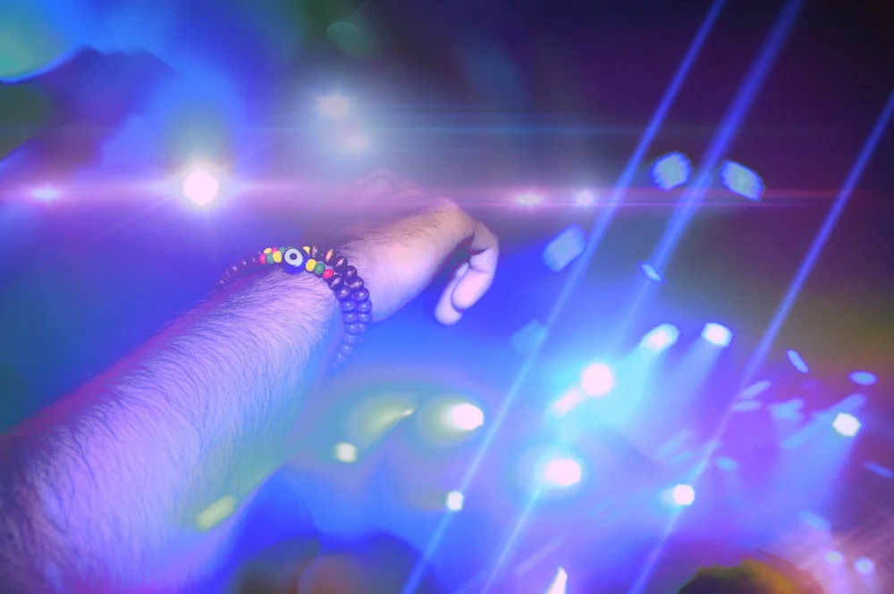 A raised arm with beaded bracelets under blue concert lights.