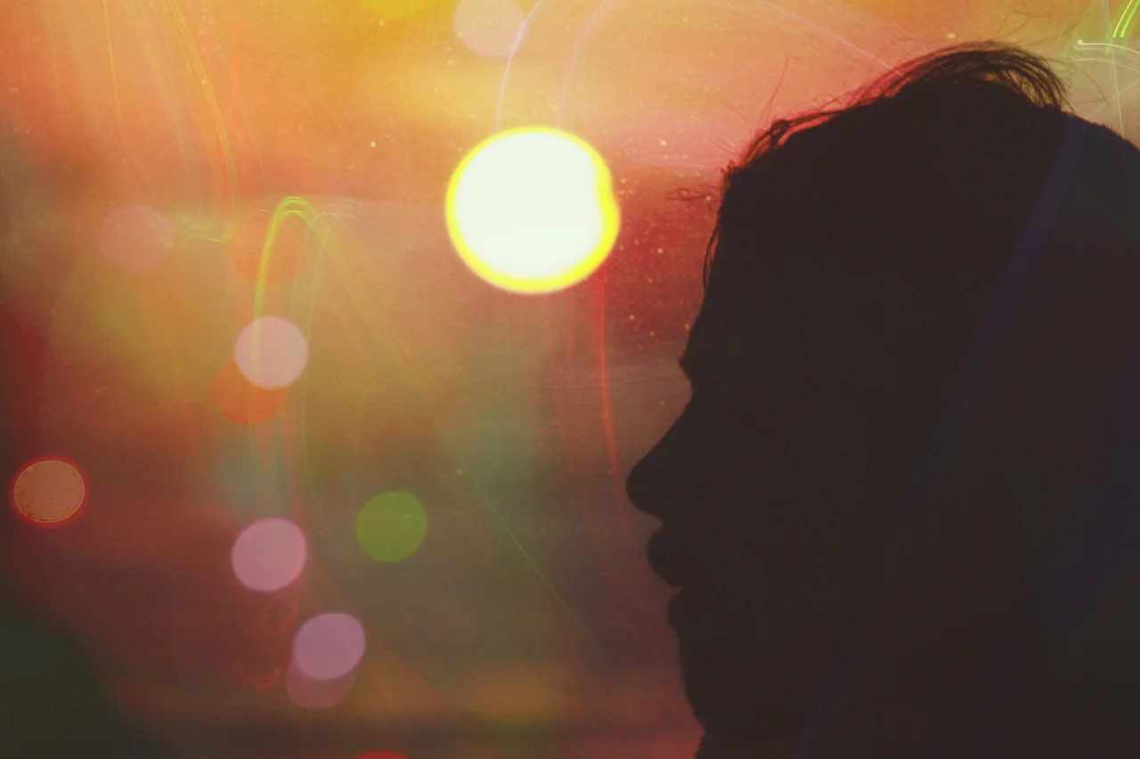Silhouette of a man's face in profile against a vibrant sunset with colorful bokeh and light streaks.