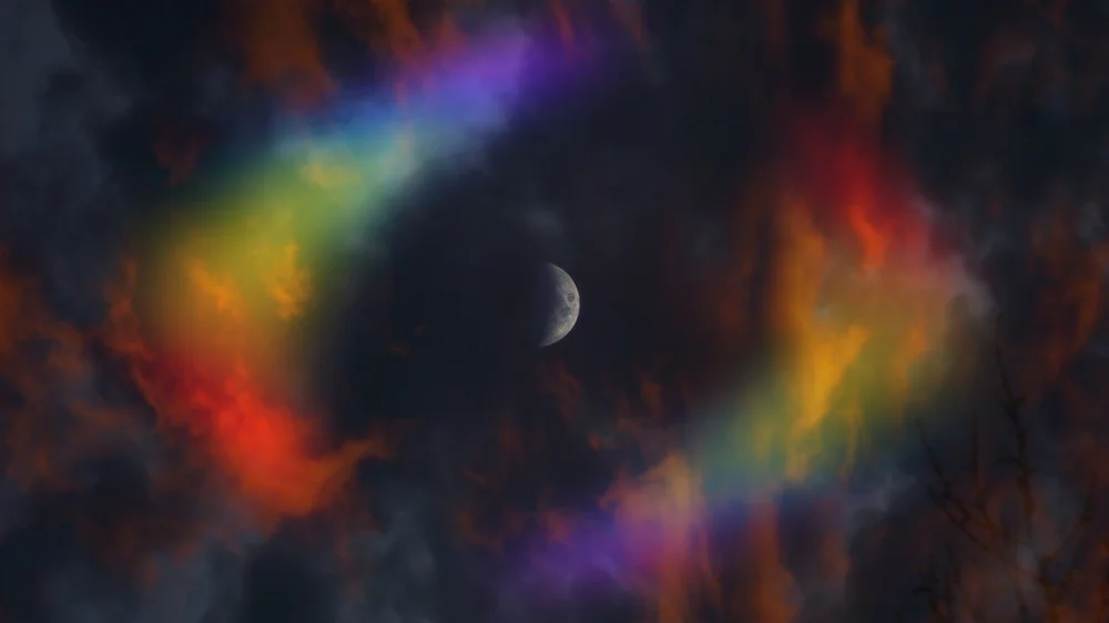 Rainbow-colored light streaks around a crescent moon in a dark sky.