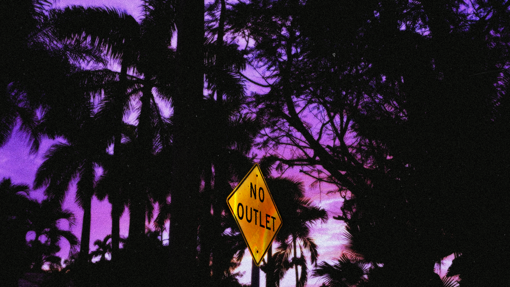 Tree silhouettes and a yellow No Outlet sign against a purple sky.