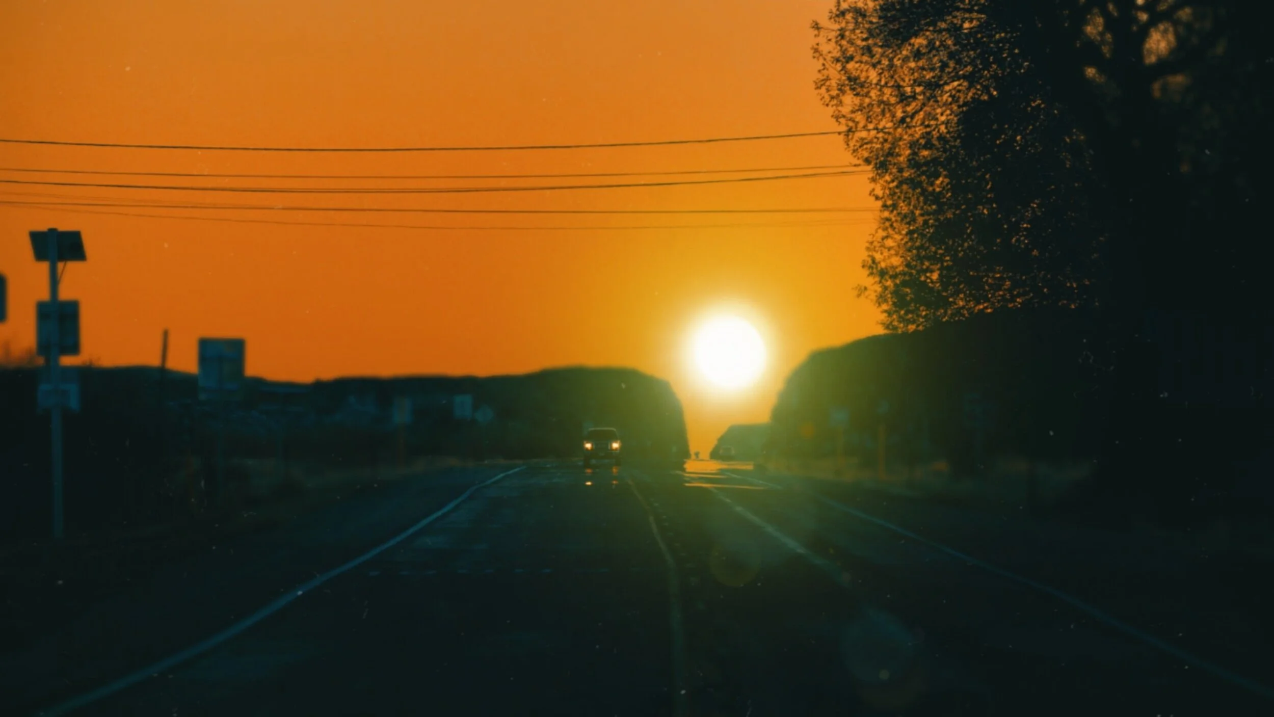 The sun setting at the end of a road lined with power lines and trees.
