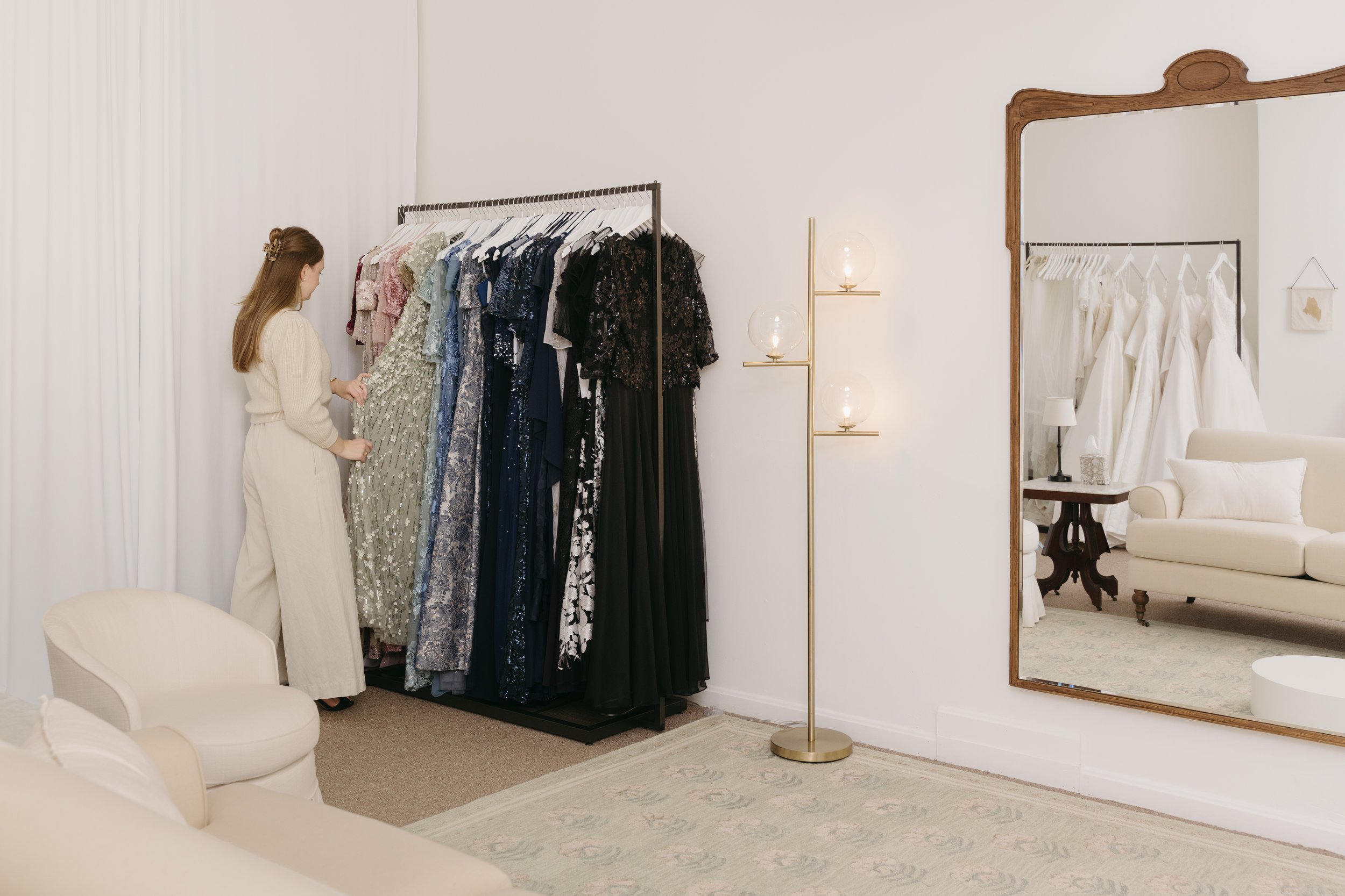 A woman shopping for dresses in a boutique, looking at a rack of formal and evening gowns.