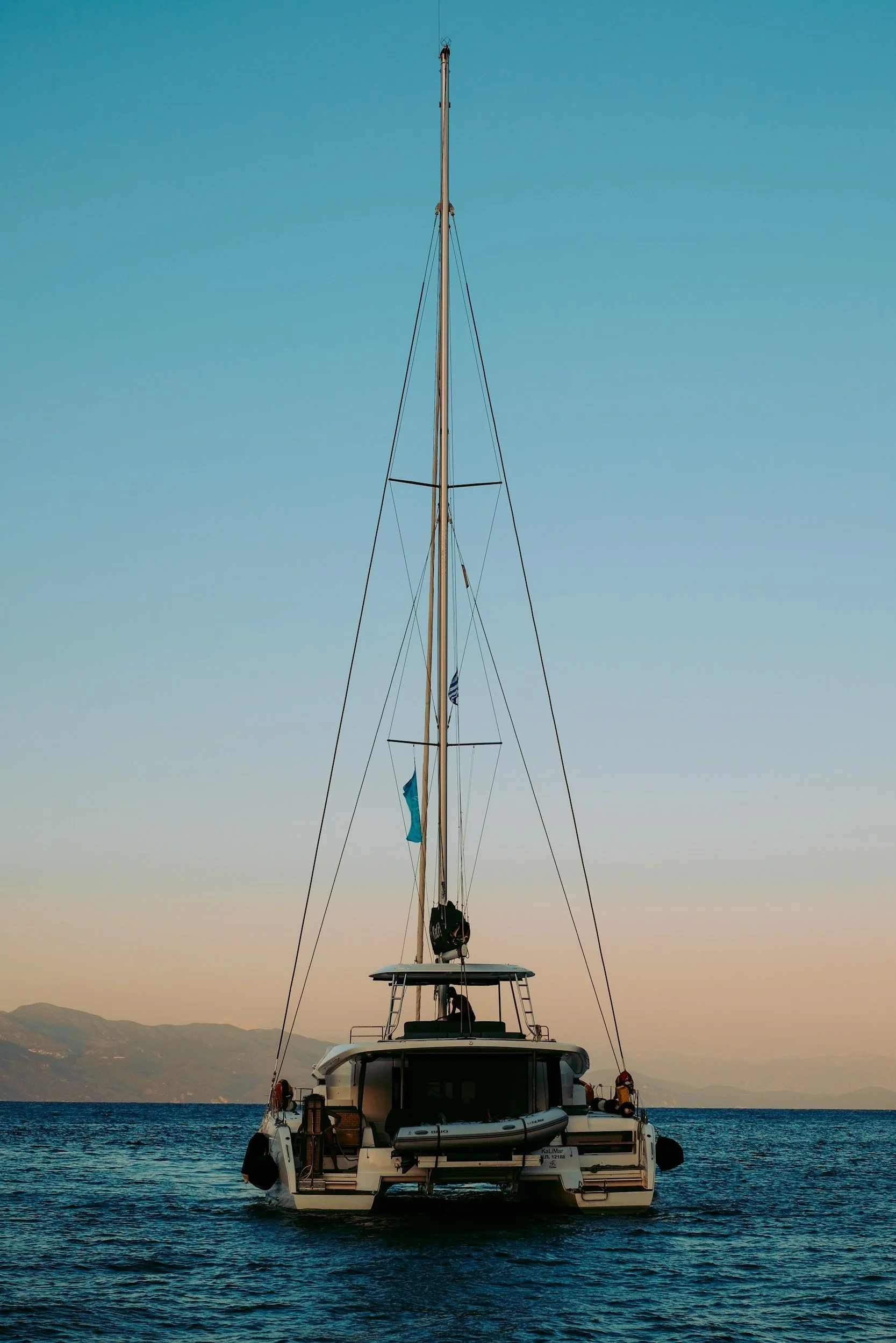 A sailboat in the water with a mountainous landscape in the background during sunset or sunrise.