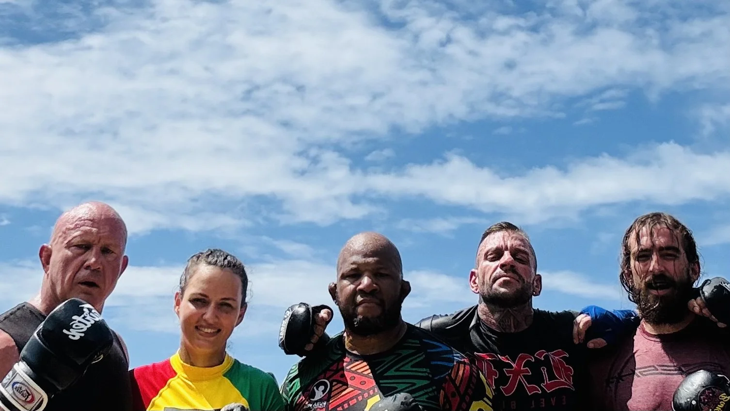 Group of five mixed gender athletes with boxing gloves, outdoors against a blue sky with clouds.