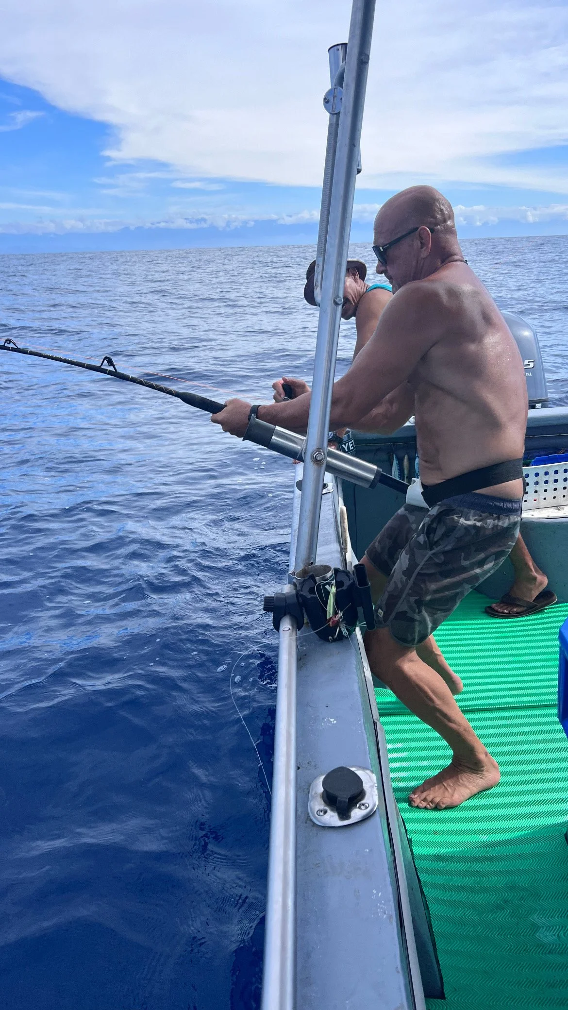 Two men fishing off a boat on the ocean, with a cloudy sky overhead.