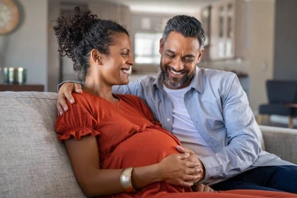 Pregnant woman sitting with partner caressing her baby bump