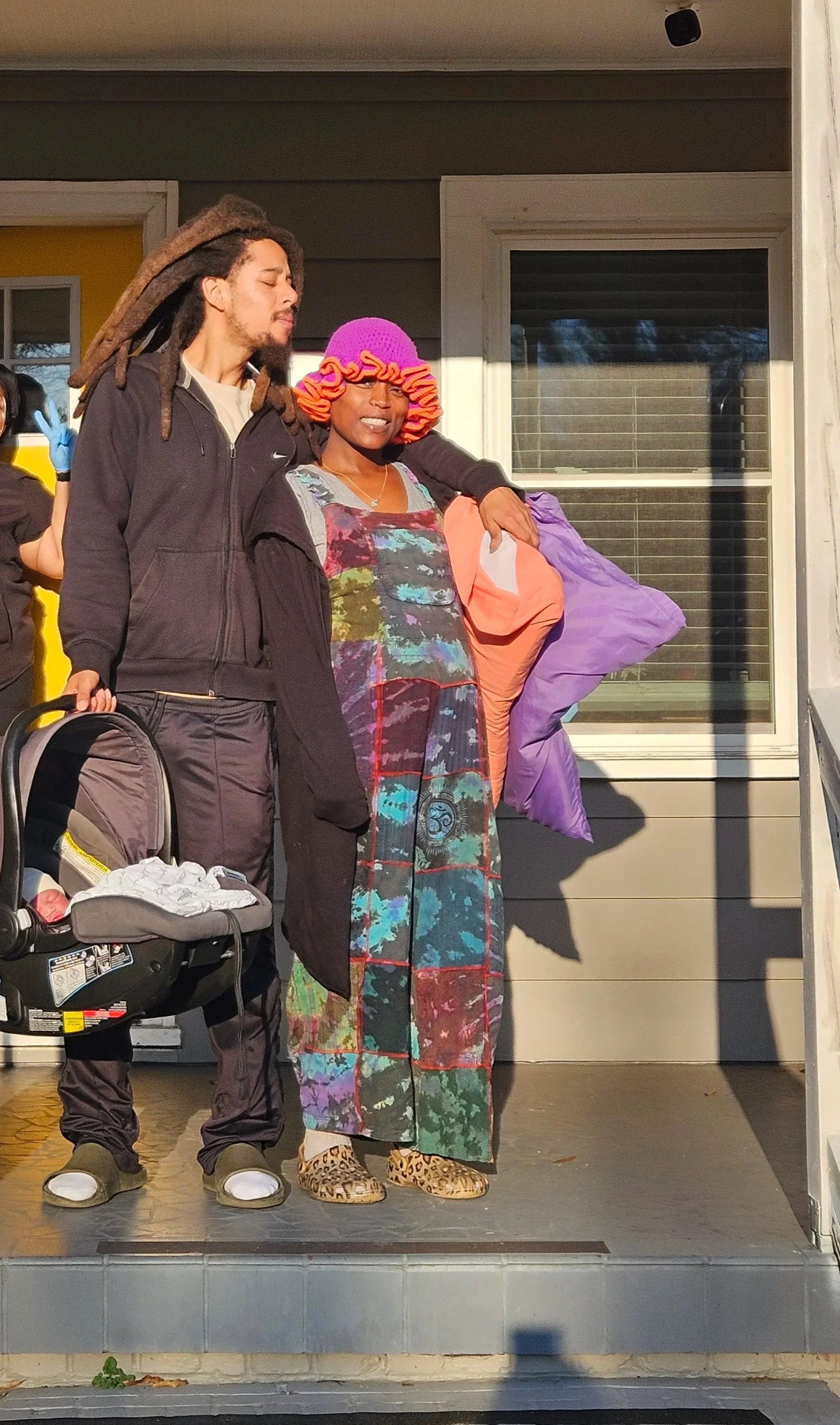Man and woman stand outside of birth center with newborn baby in a carseat