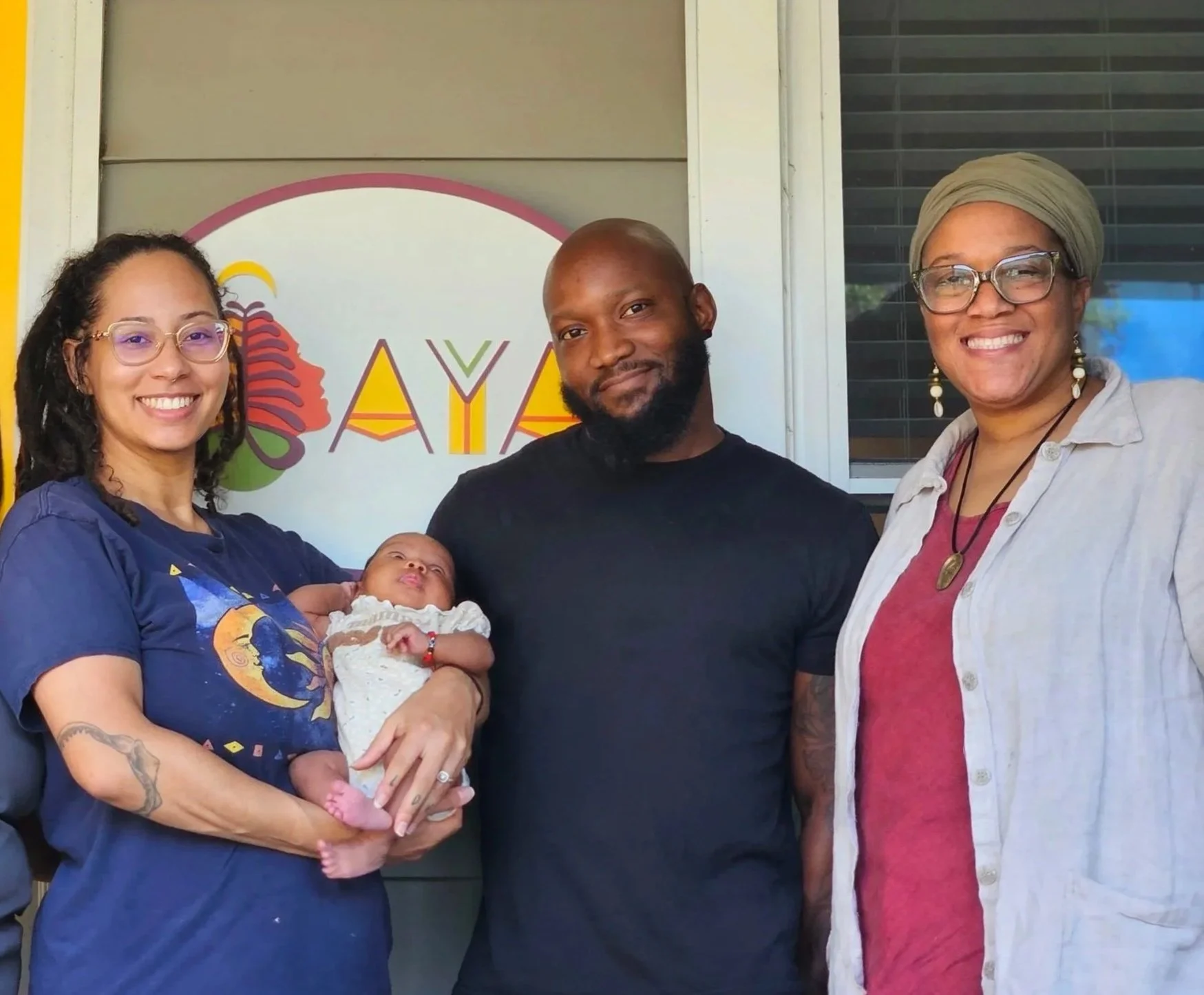 Mother holding newborn baby with father and midwife outside of birth center