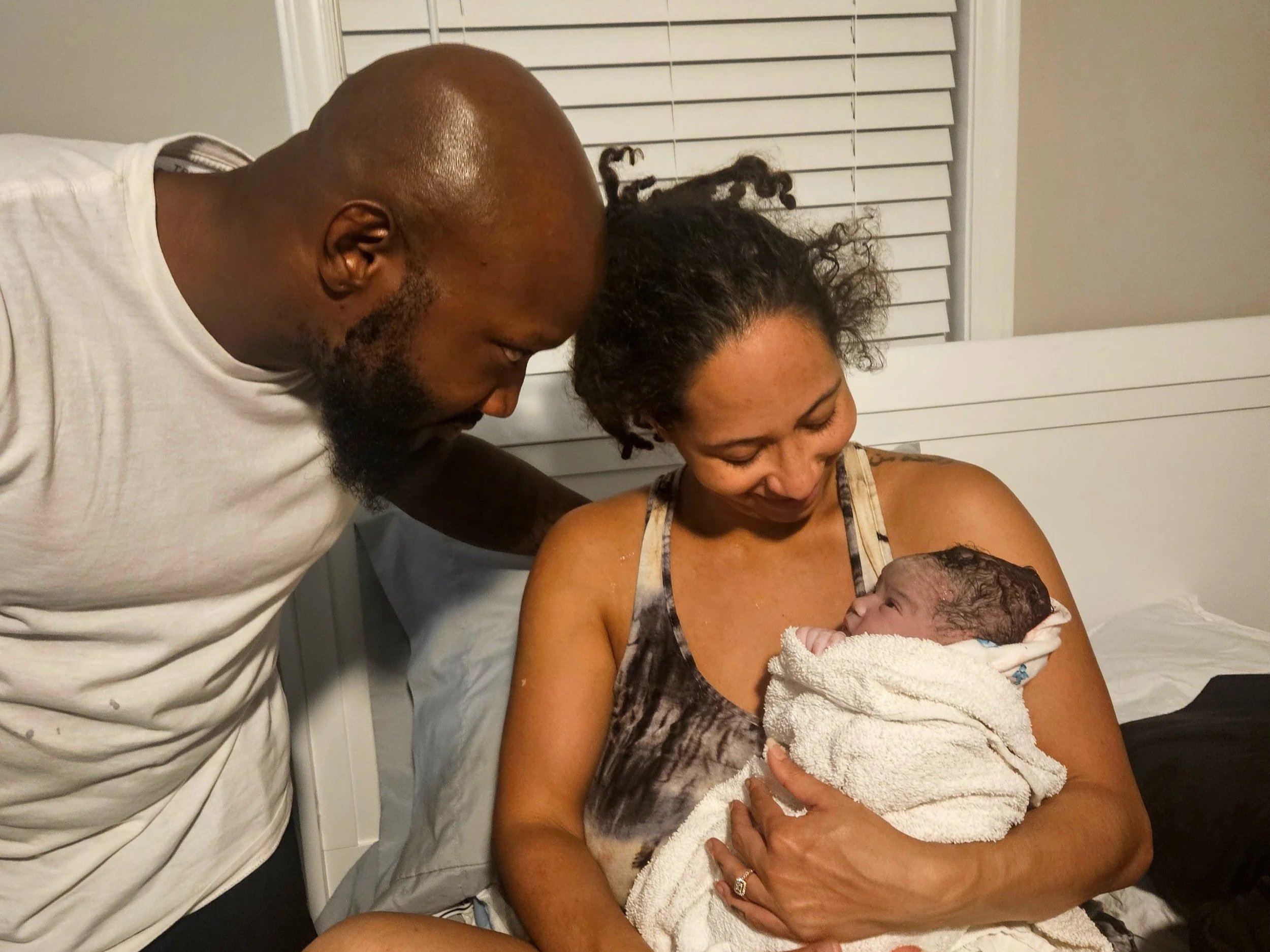 Woman holds newborn baby while partner looks on in birth center