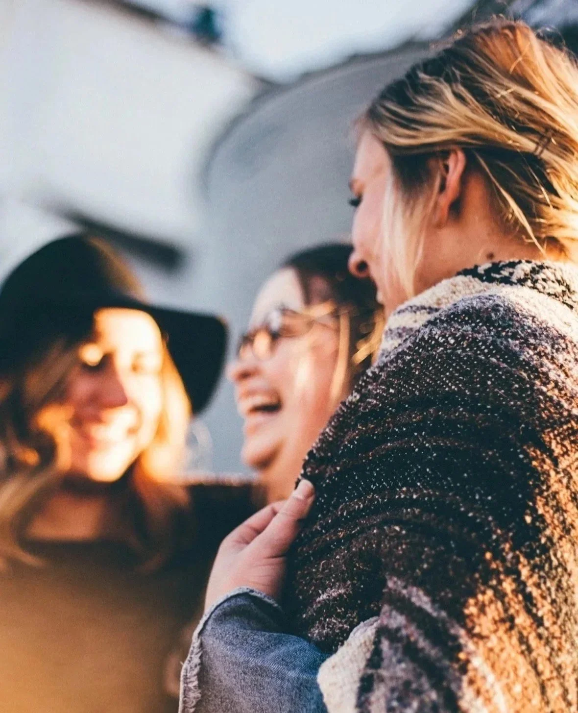 Three people smiling and laughing close together, one person touching another's shoulder,  during a group therapy session in daytime.