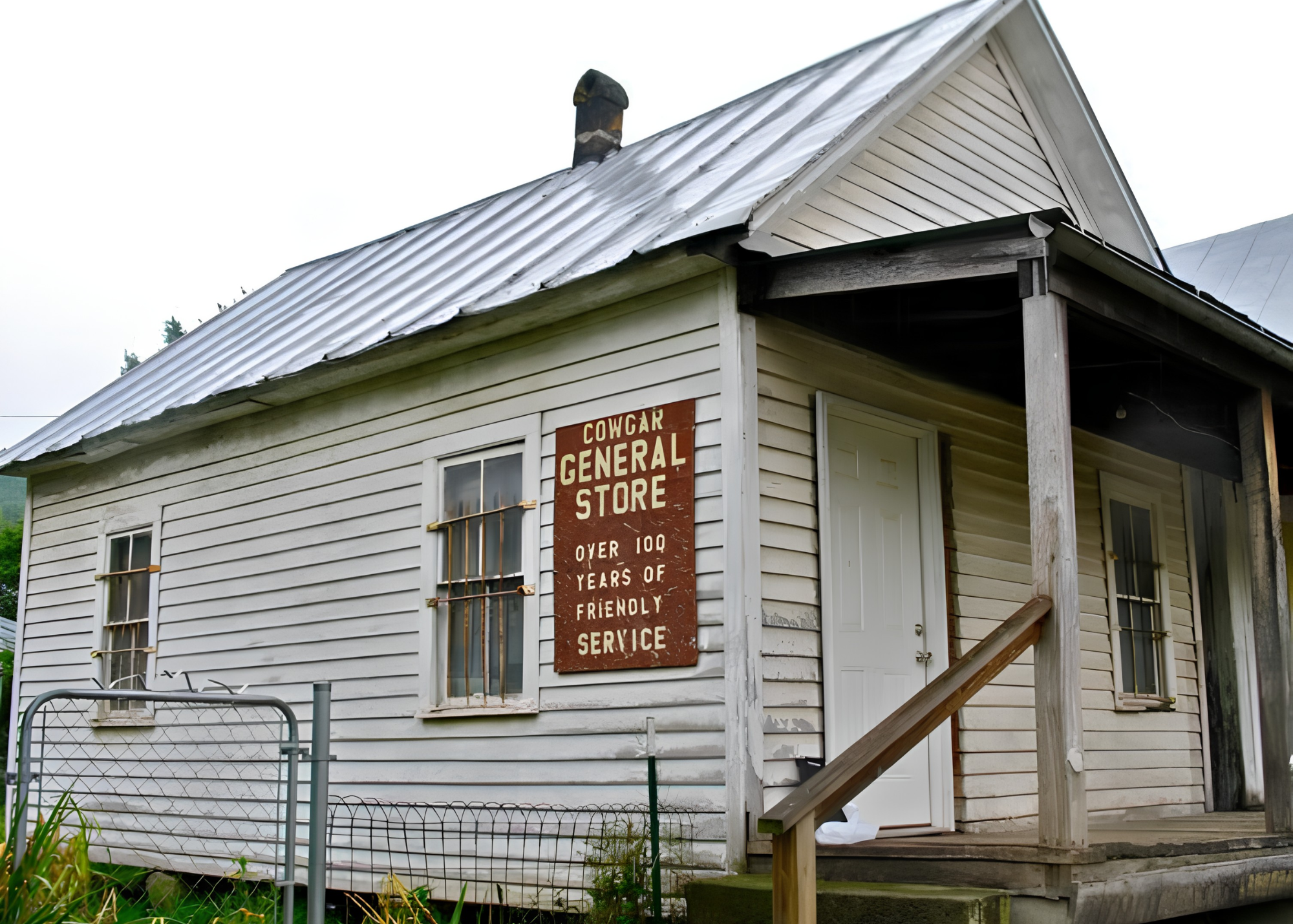A small, weathered wooden building with a metal roof and a porch. There is a sign on the front that reads 'Cowcar General Store Over 100 Years of Friendly Service.'