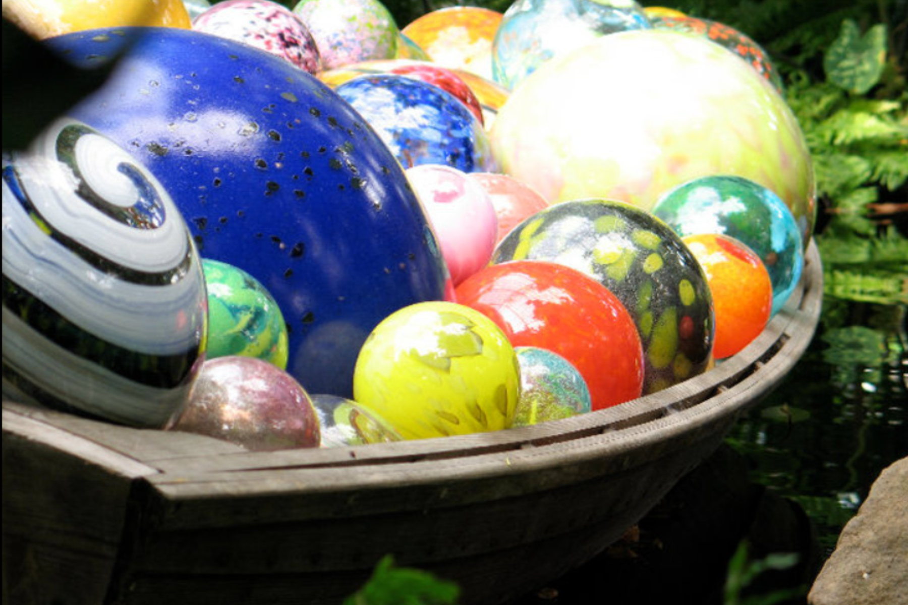 Colorful glass marbles inside a wooden bowl outdoors.