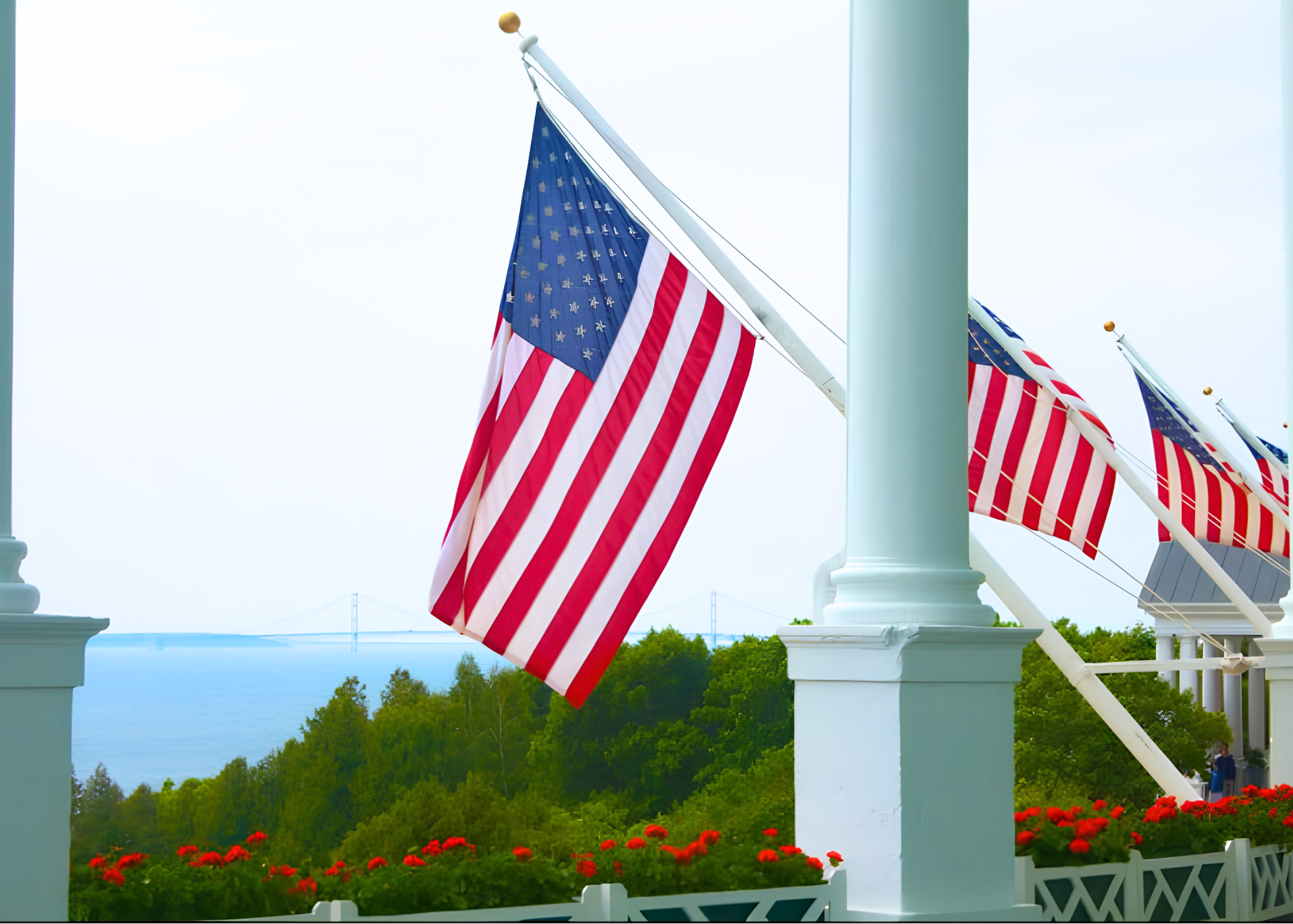 American flags on a porch with a scenic background of trees, water, and a bridge.