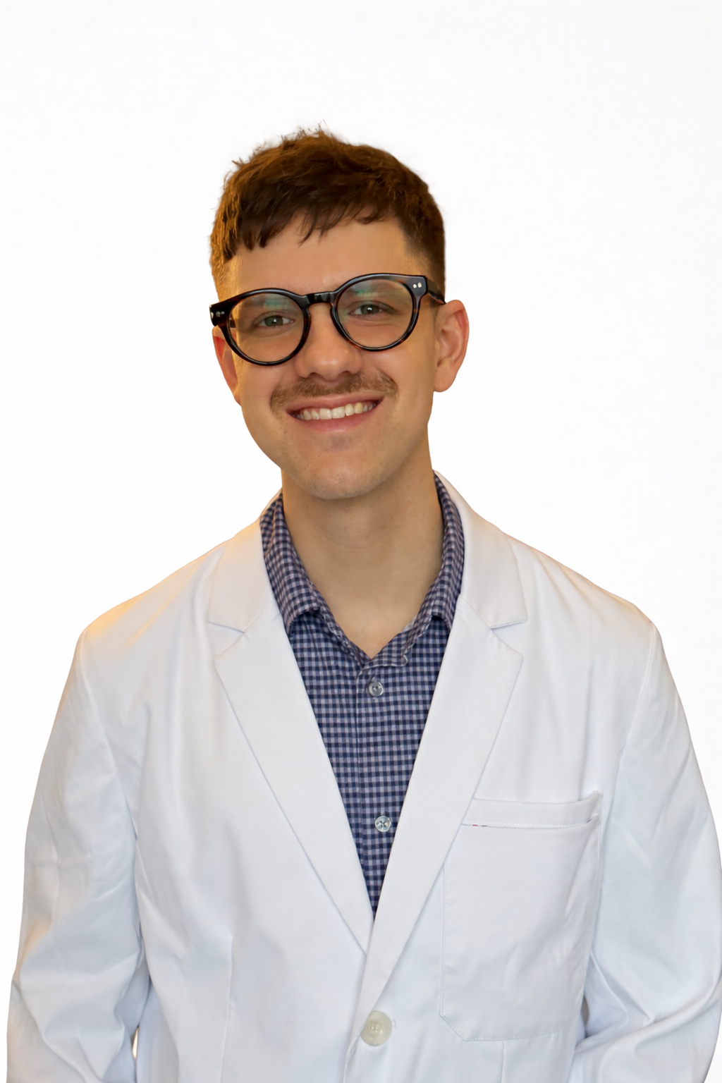 A smiling man wears black glasses, a white doctor's coat, and a blue checkered shirt against a plain white background.