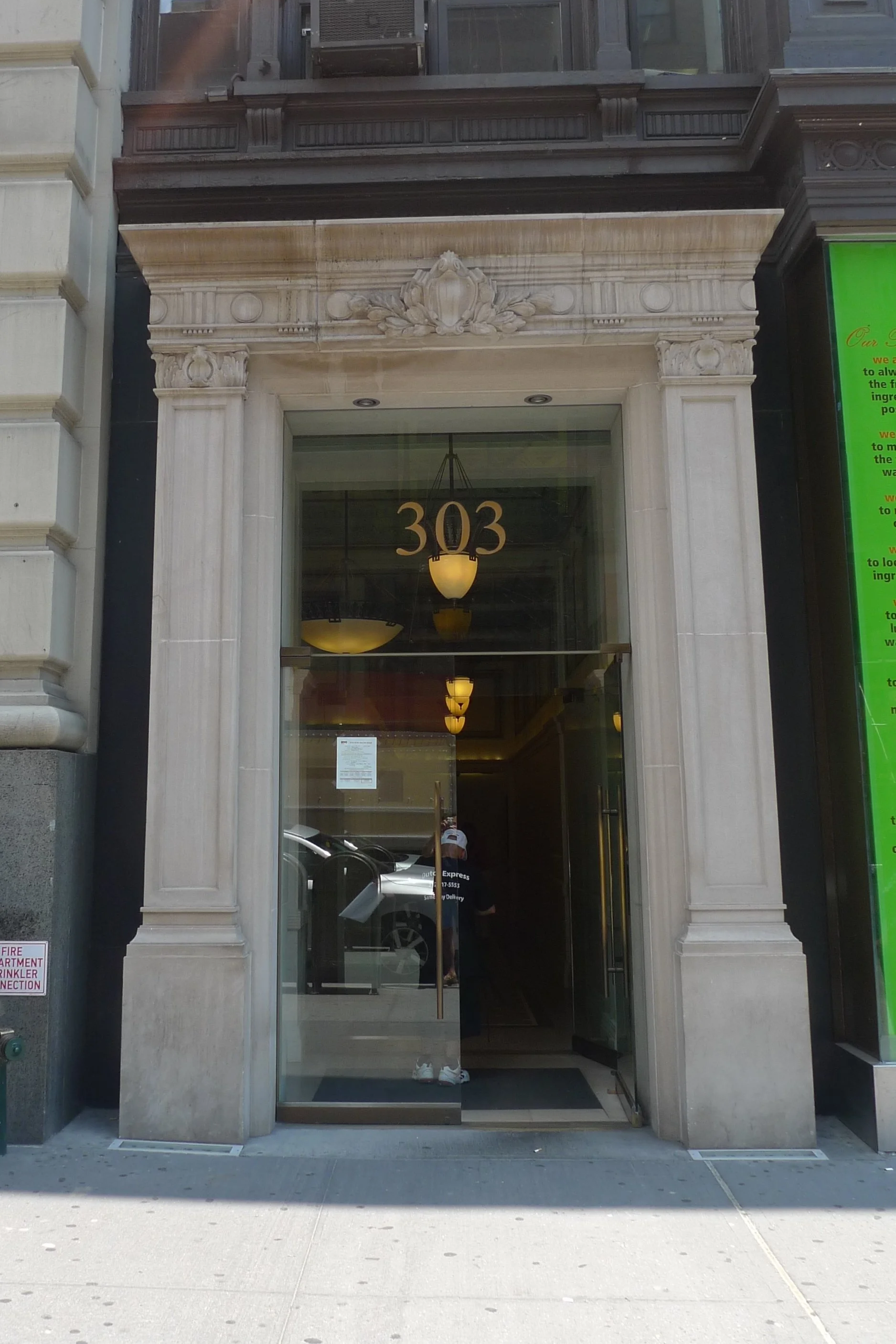 Exterior view of a building with the street number 303 above the entrance, featuring large glass doors and a decorative stone frame.