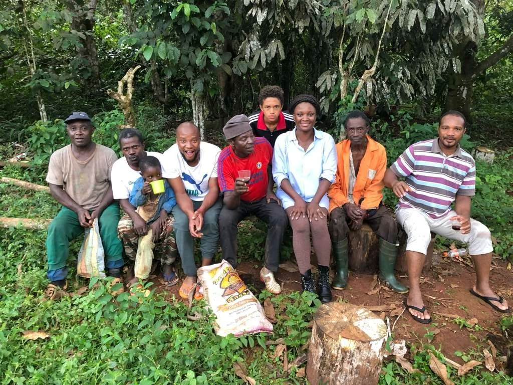A group of ten people, including children, sitting on a log and a tree stump in a lush green forest. They are posing for the photo, some smiling and others looking at the camera.