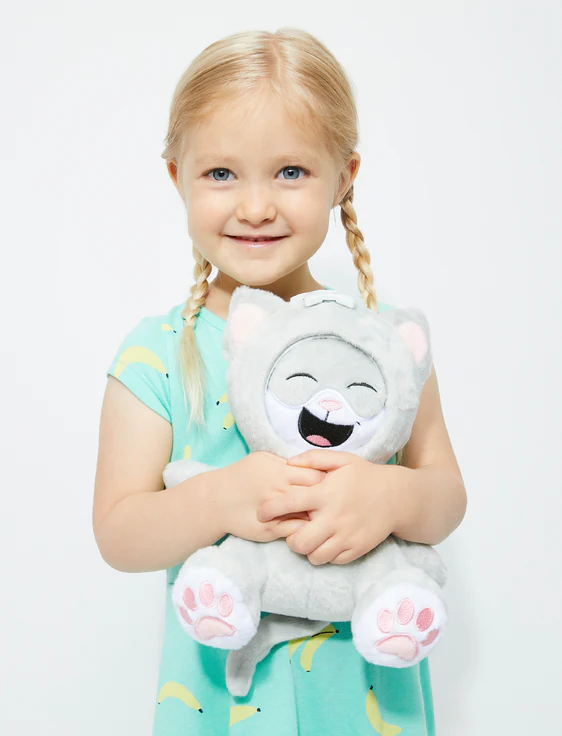 A young girl with blonde hair in braids and blue eyes holding a gray plush toy cat with a happy face.