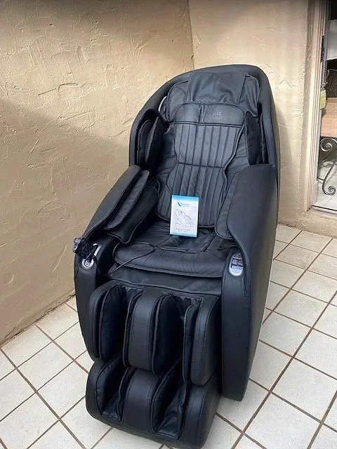 A black massage chair on a tiled floor next to a beige wall with a tag on it.