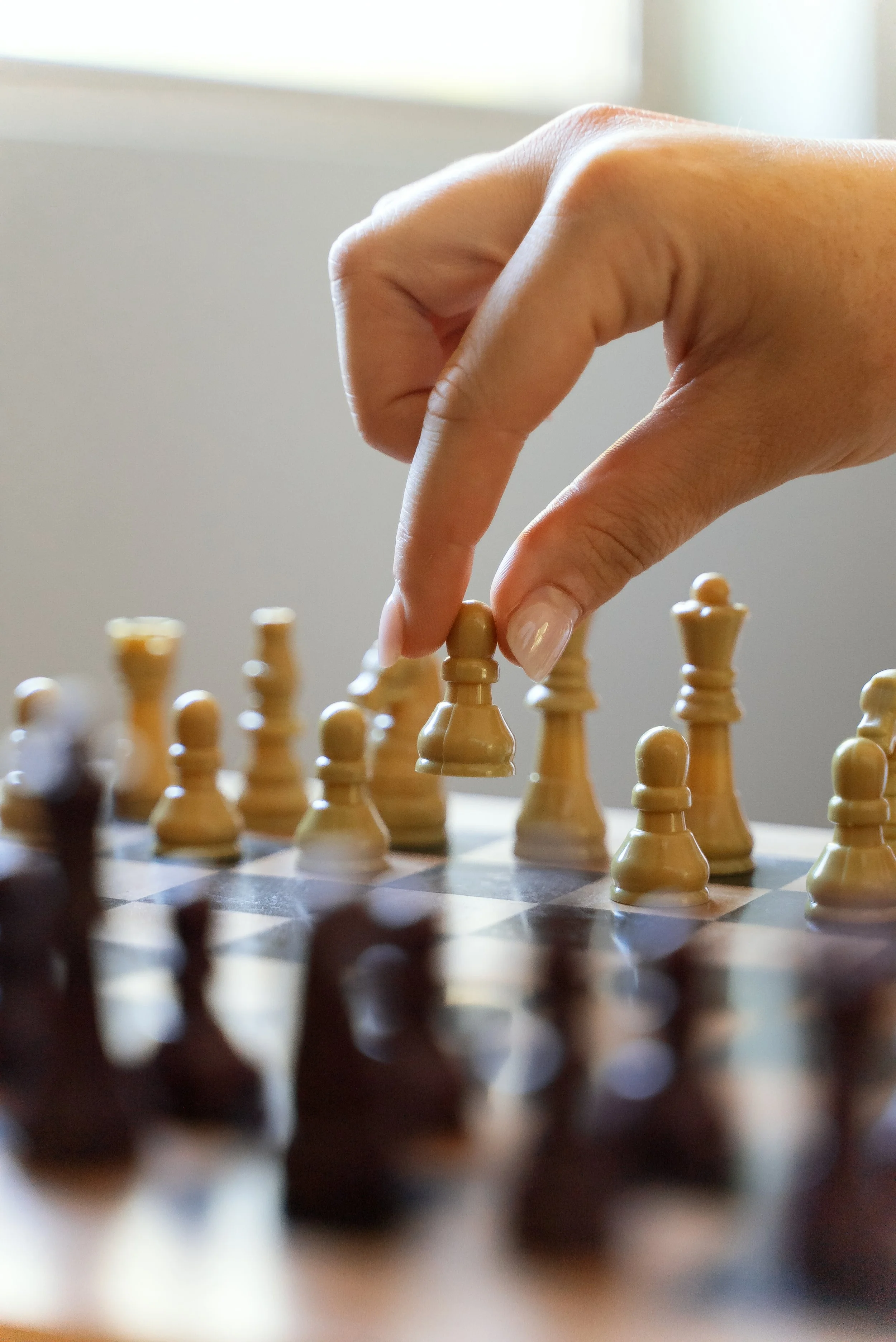 A person moving a white chess piece on a chessboard during a game.
