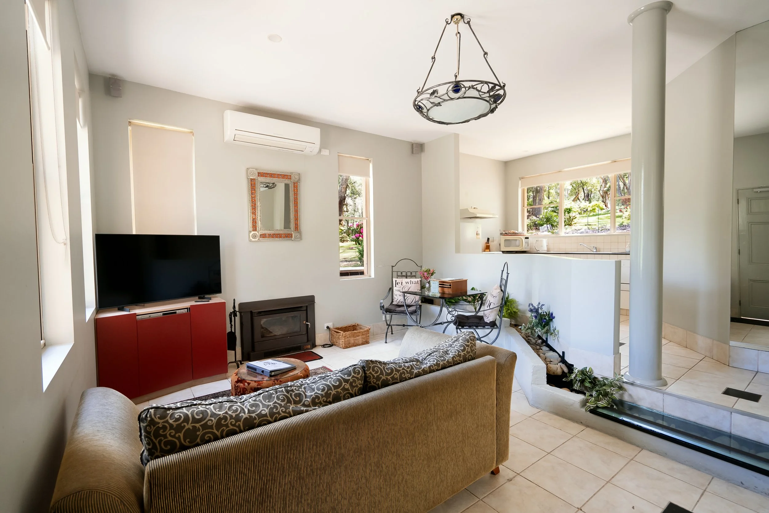 Living room with a sofa, armchair, television, fireplace, and kitchen opening, with large windows.