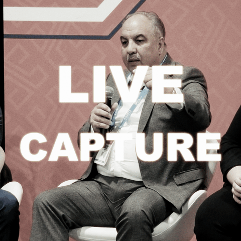 Man in a gray suit speaking into a microphone during a panel discussion.