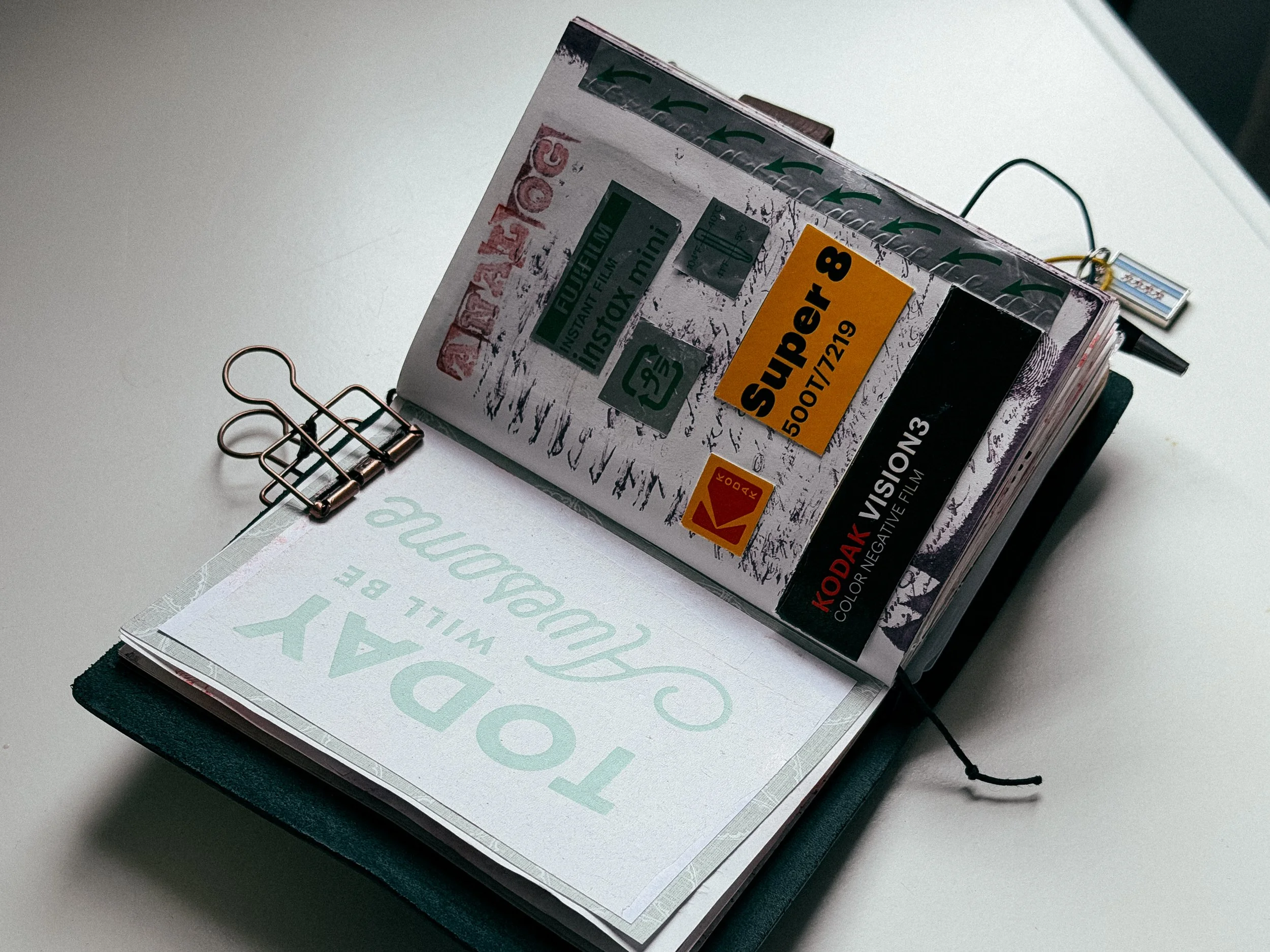Stack of printed photographs or film negatives, bound by a metal paper clip, with a black string bookmark, lying on an open book or folder with printed text.