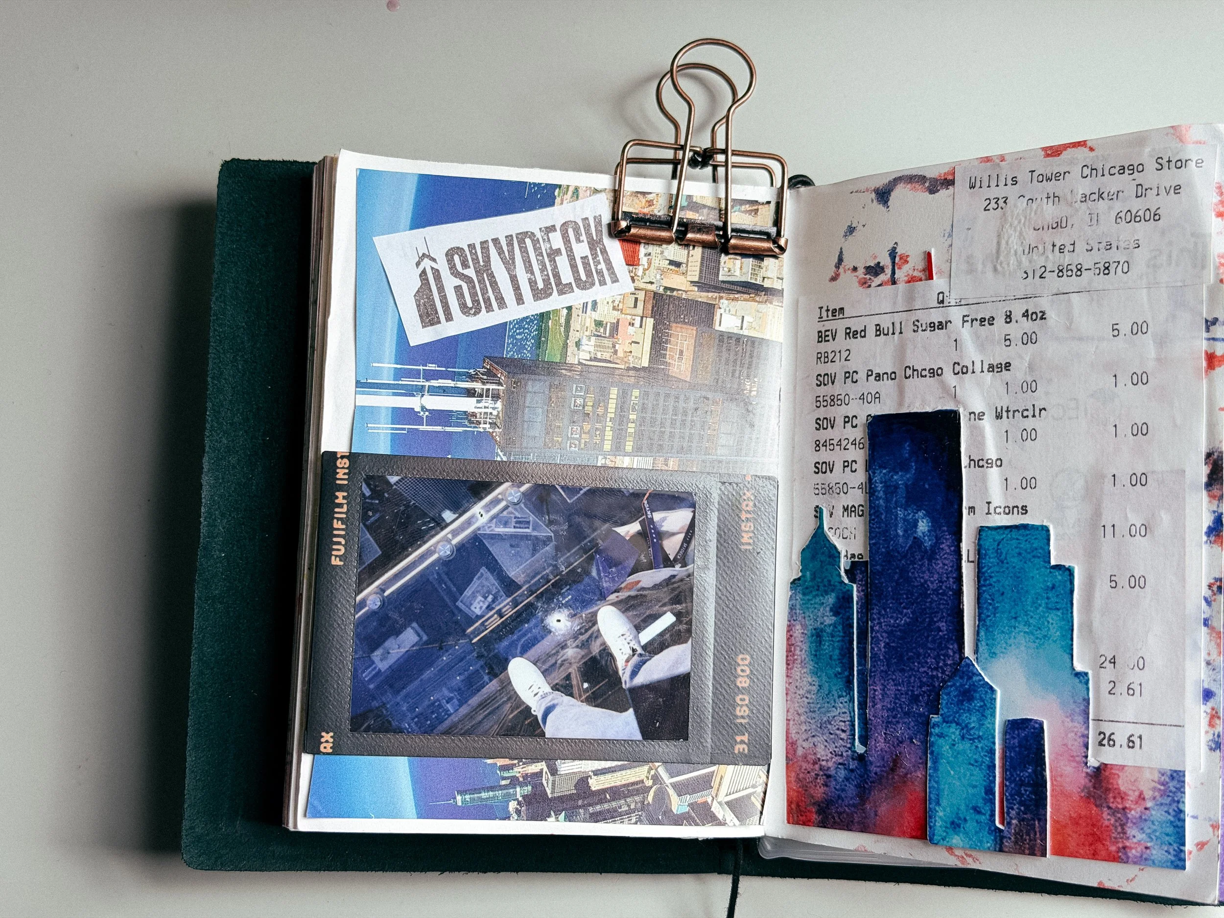 Open travel guidebook featuring images of Chicago skyscrapers, cityscape, and a large binder clip holding the pages, with a receipt partially covering the right page.