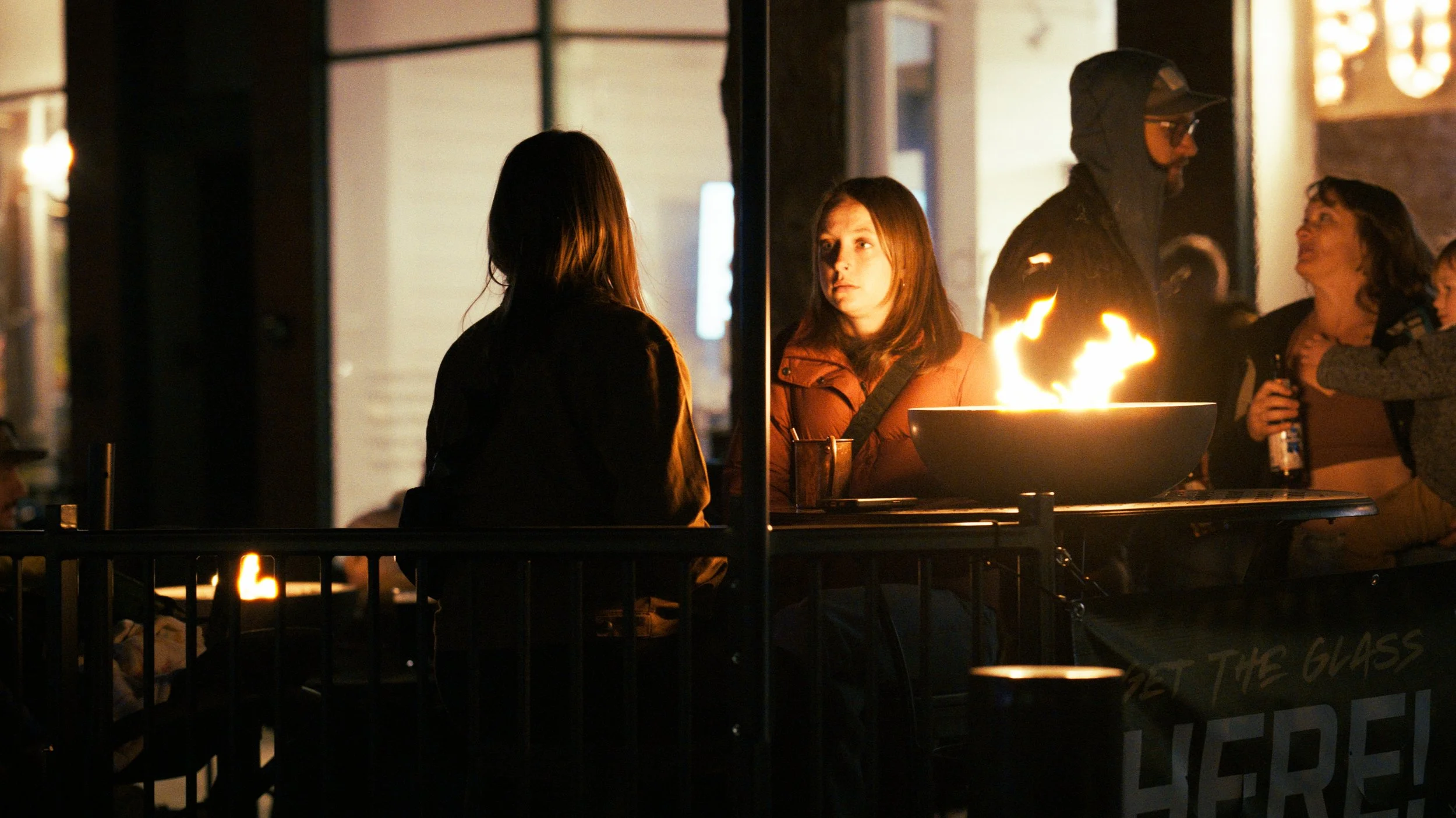 People gathered around a fire pit outside at night, engaged in conversation and laughter.