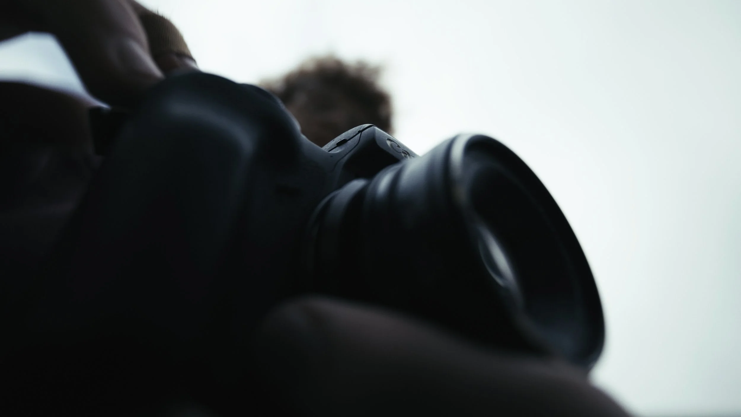 Close-up of a person holding a camera, viewed from below against an overcast sky.