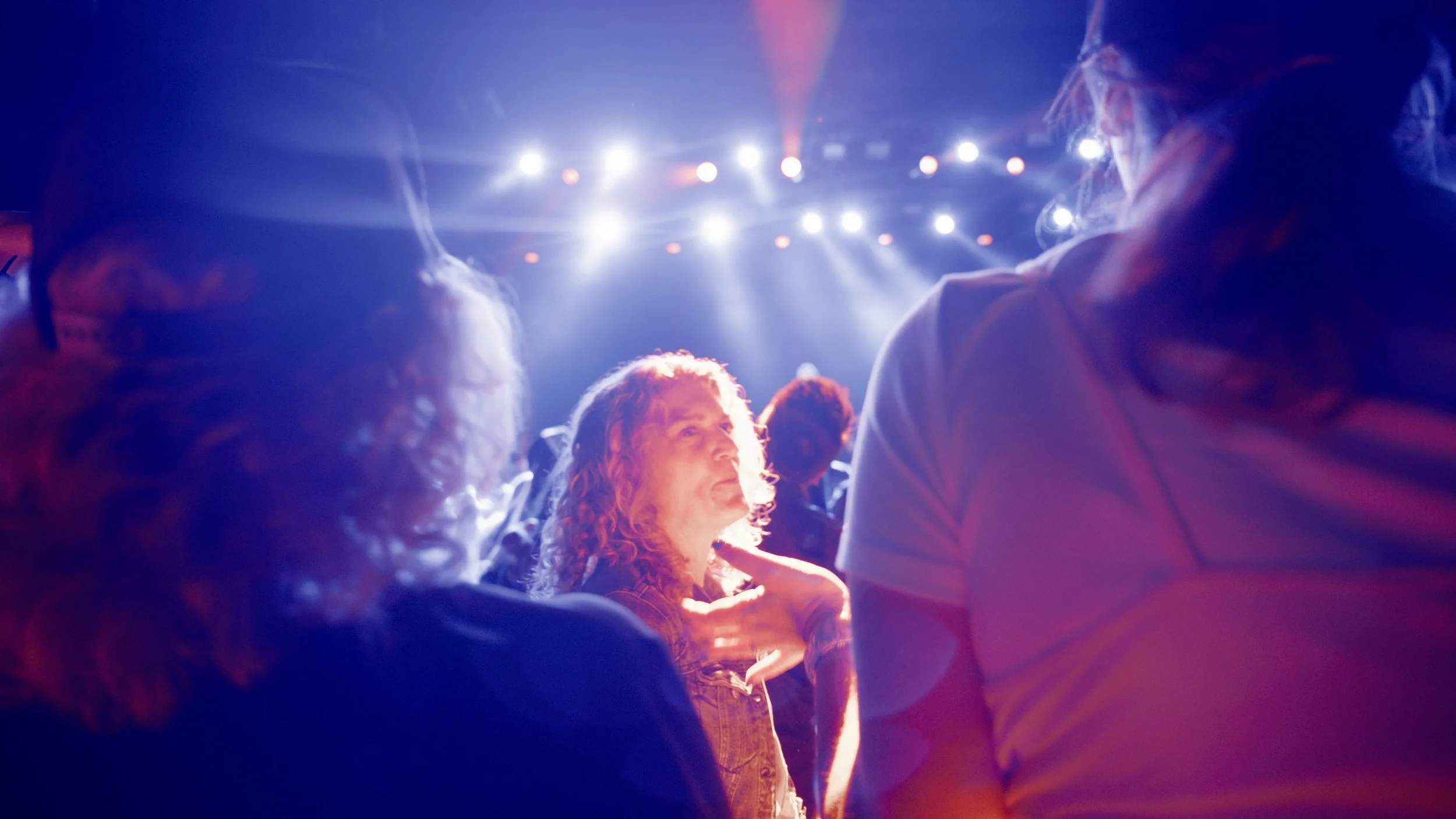 Audience sitting in a dimly lit venue, illuminated by bright stage lights for a concert or event.