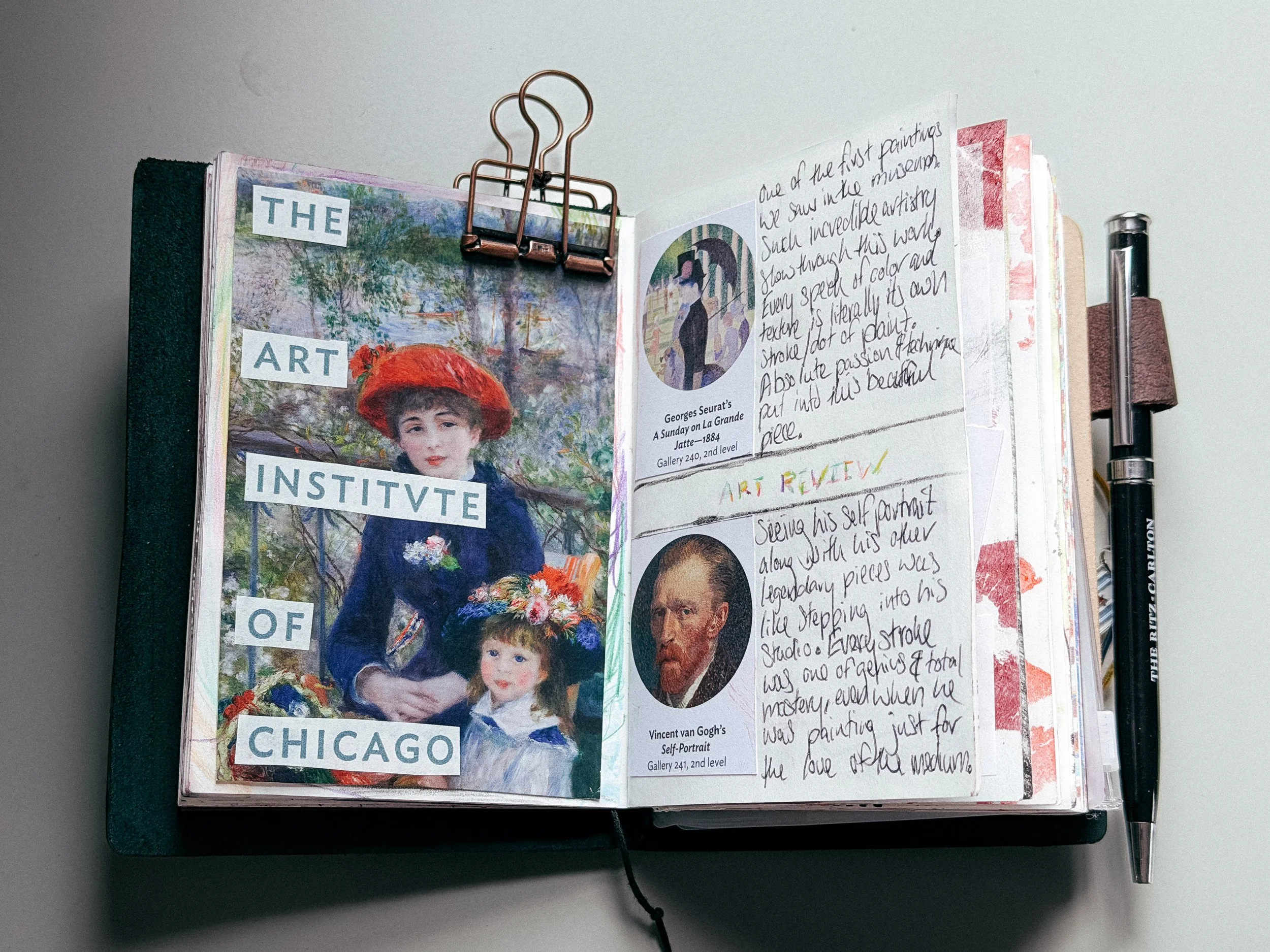 Open sketchbook or art journal with a collage of artwork and handwritten notes, clipped to the top with a paper clip, with a black pen placed on the right side.