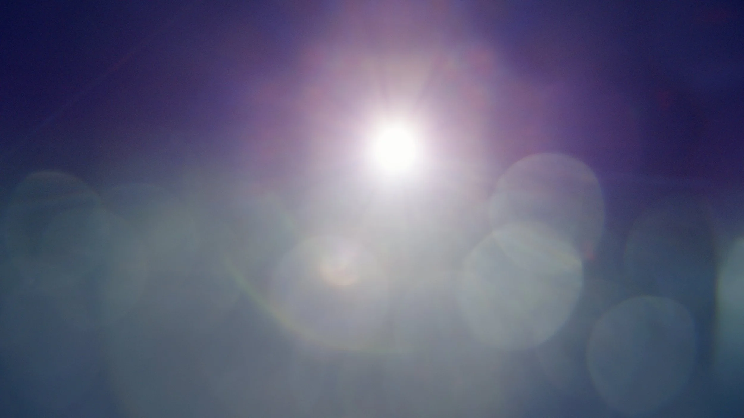 Bright sunlight with lens flare against a clear blue sky.