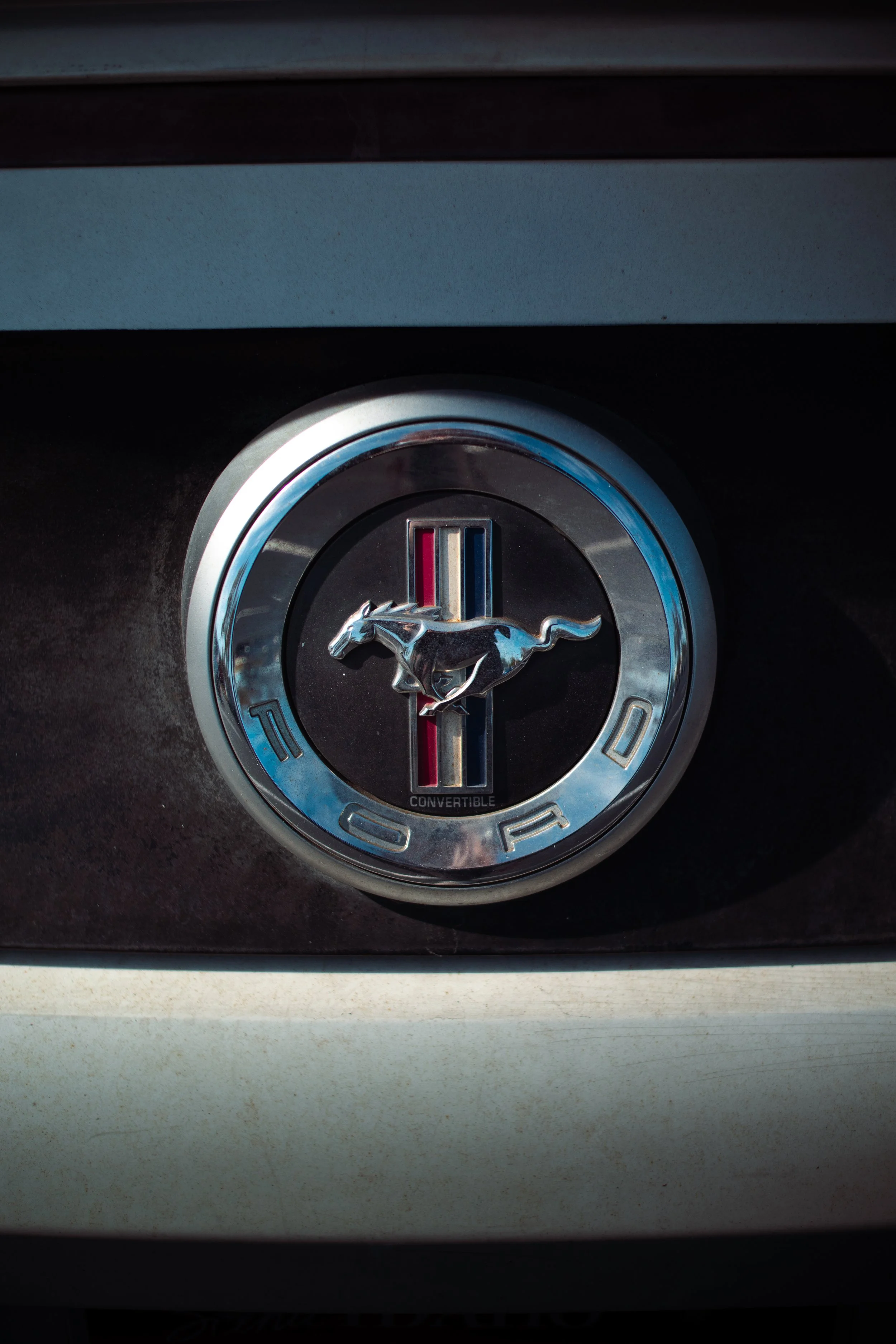 Close-up of a Ford Mustang emblem on a vehicle, featuring the running horse logo and a blue, white, and red racing stripe.