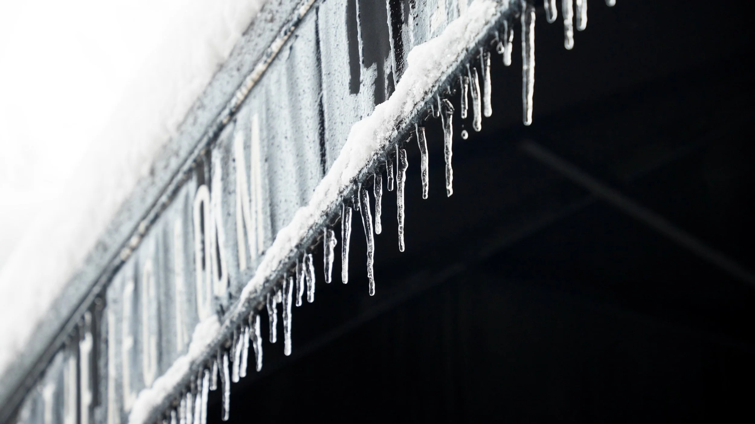 Icicles hanging from the edge of a snow-covered surface against a dark background.