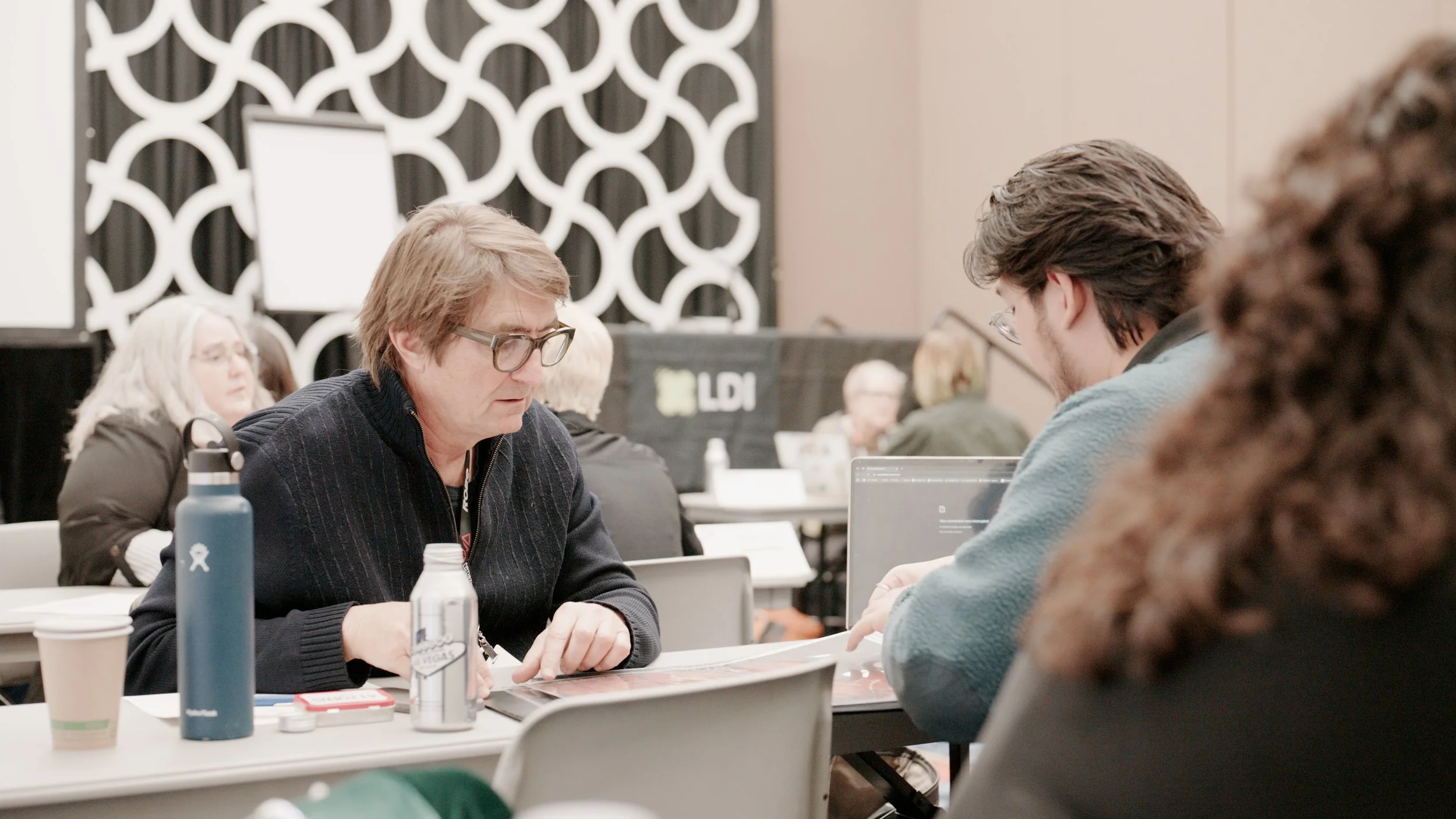 People seated at a table engaged in conversation or a discussion in a conference room with modern decor and a decorative wall behind them.