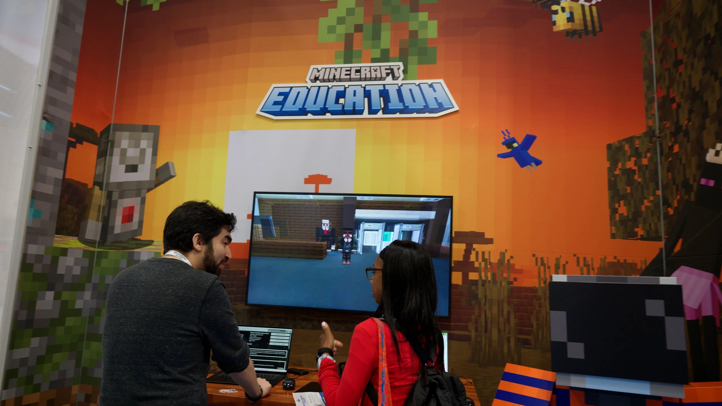 People talking at a booth with a Minecraft-themed background showcasing pixelated characters and the words 'Minecraft Education'.